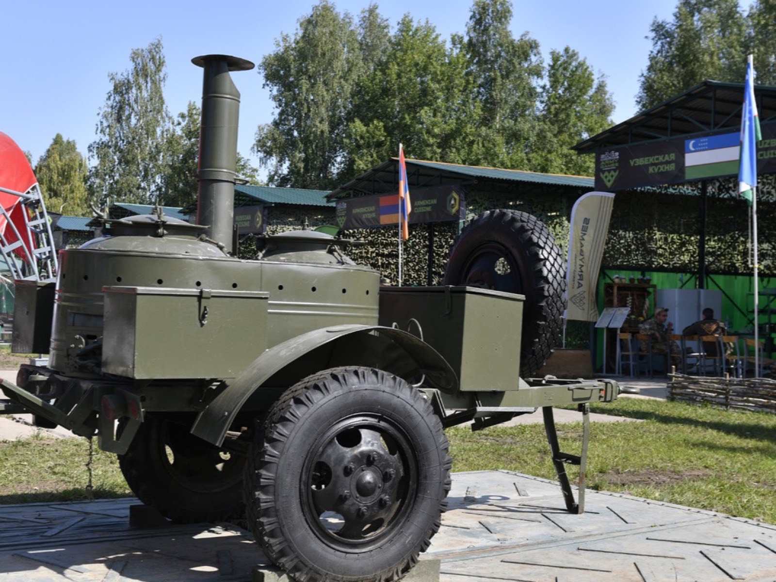 Полевая кухня на прицепе с трубой и двумя котлами на площадке конкурса «Полевая кухня»; позади павильоны с флагами